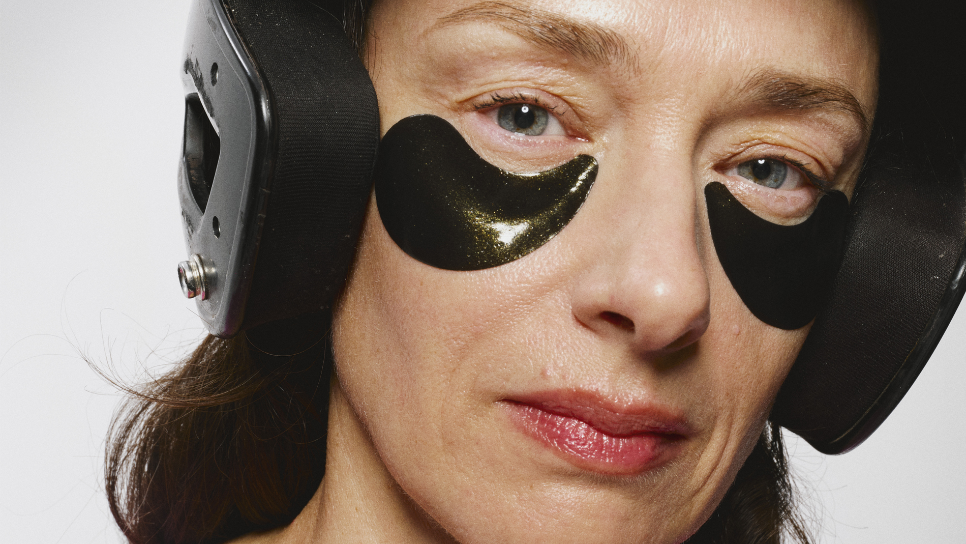 Henkilö, jolla on pitkät tummat hiukset ja vaaleanpunainen paita, ja joka käyttää mustaa kypärää ja mustia eye patches silmien alla