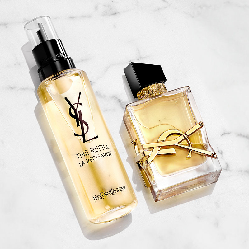 To parfymeflasker fra Yves Saint Laurent på en hvit marmorbakgrunn. Den ene flasken er en refillflaske med YSL-logoen i svart. Den andre flasken er gjennomsiktig med gullfarget væske og har YSL-logoen i gull og en svart kork.
