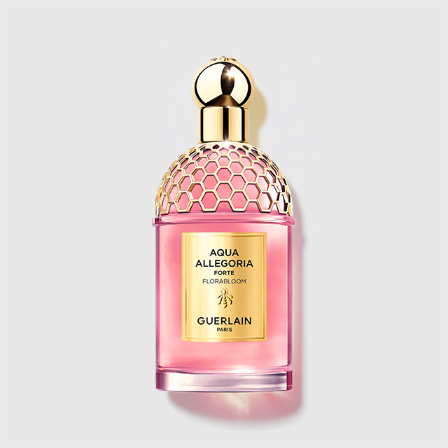 Guerlain Aqua Allegoria Forte Flora Bloom parfyme i en rosa flaske med gullfarget bikubemønstret kork og etikett. På flasken står “AQUA ALLEGORIA FORTE FLORA BLOOM GUERLAIN PARIS”.