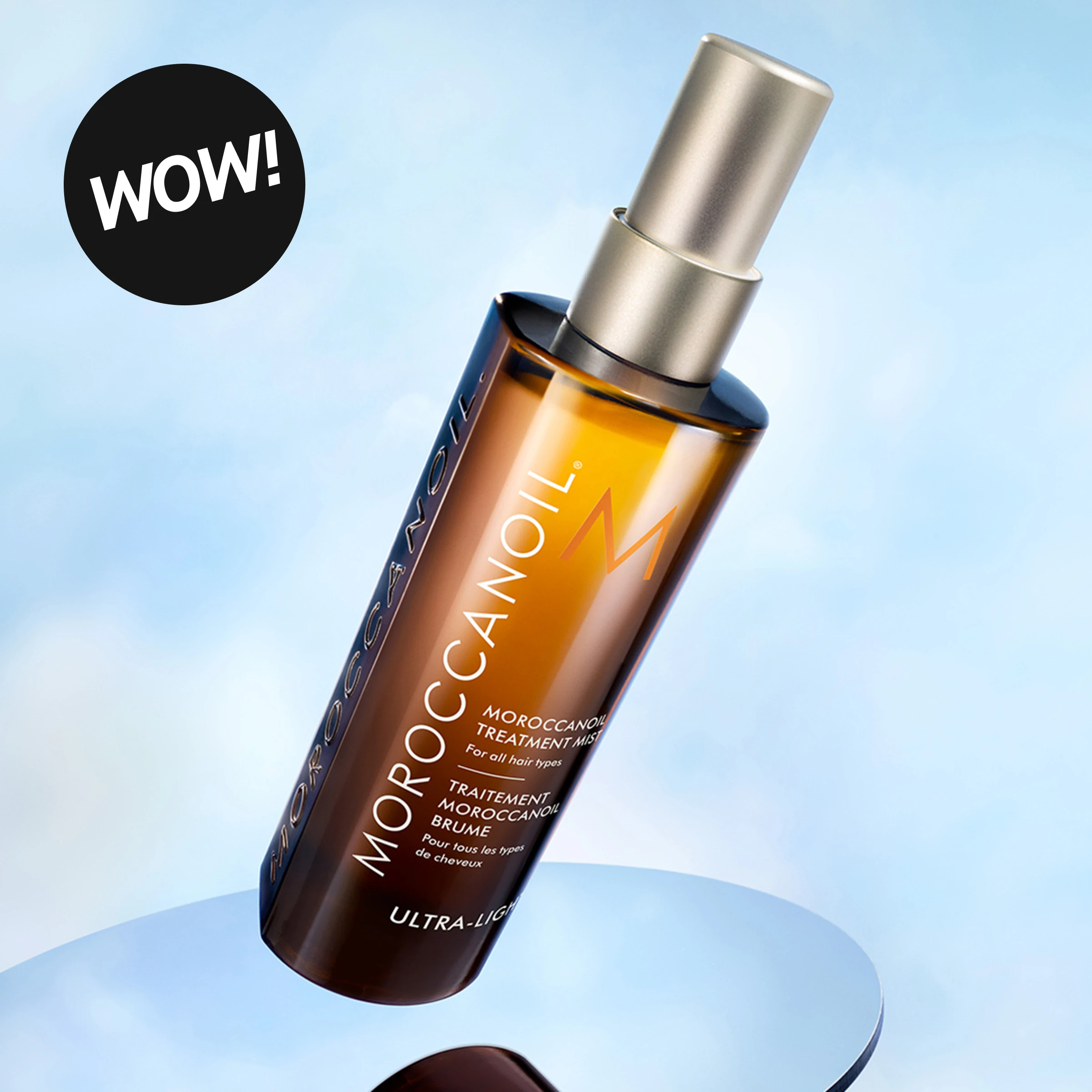 Moroccanoil Treatment Mist Ultra-Light på en blå pidestall mot lys blå bakgrunn. På flasken vises tekstene «MOROCCANOIL», «TREATMENT MIST», «ULTRA-LIGHT» og en svart sirkel med teksten «WOW!».