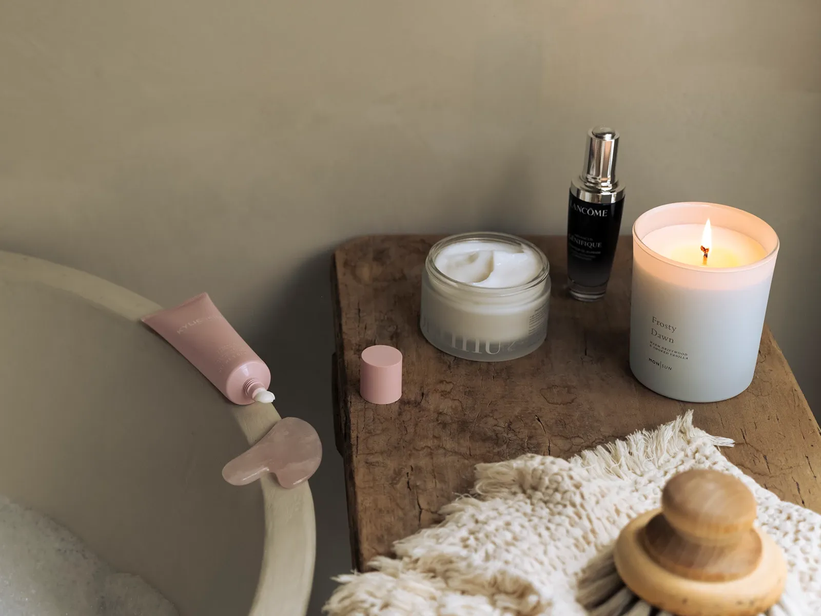 Hemmaspa-miljö med badkar, hudvårdsprodukter, tänd doftljus och en gua sha-sten på ett träbord.