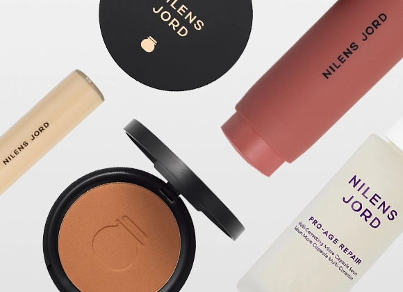 En samling av Nilens Jord skjønnhetsprodukter, inkludert en concealer, et kompaktpudder, en ansiktskrem og et ansiktsserum. Produktene er stilfullt arrangert mot en hvit bakgrunn.