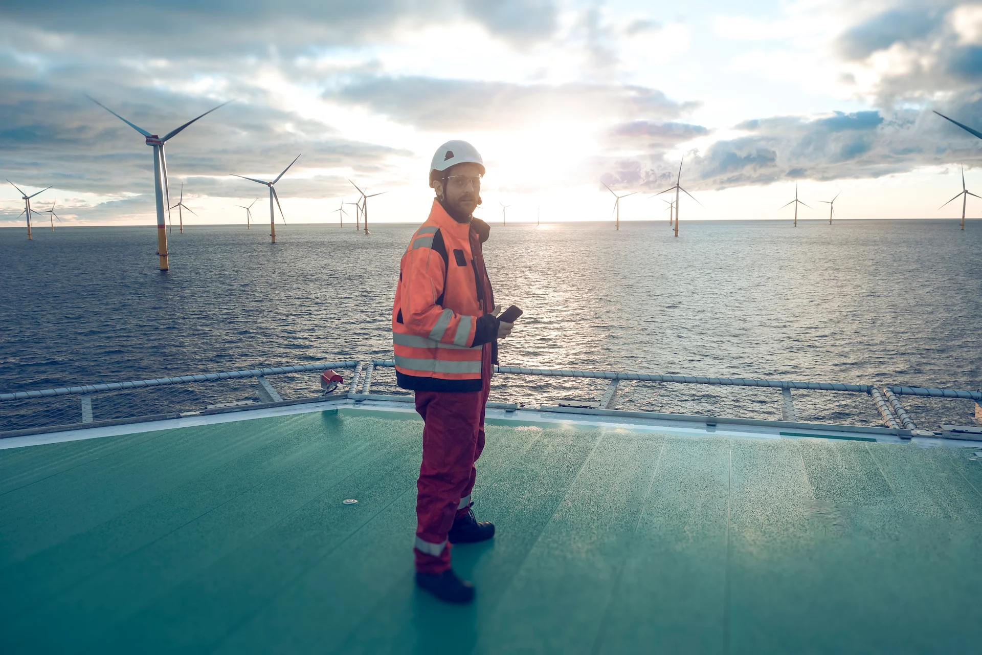 A man standing on a helipad offshore, overseeing operations and preparing for a helicopter landing amidst a dynamic marine environment.