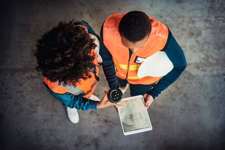 Two people in safety vests collaborate on a tablet