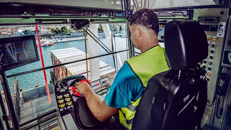Crane operator handling container cargo at a port terminal, showcasing precision and focus in operating advanced machinery for safe and efficient loading and unloading operations.