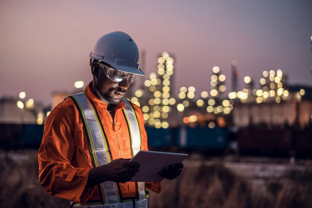 Engineer using tablet near oil refinery at night.