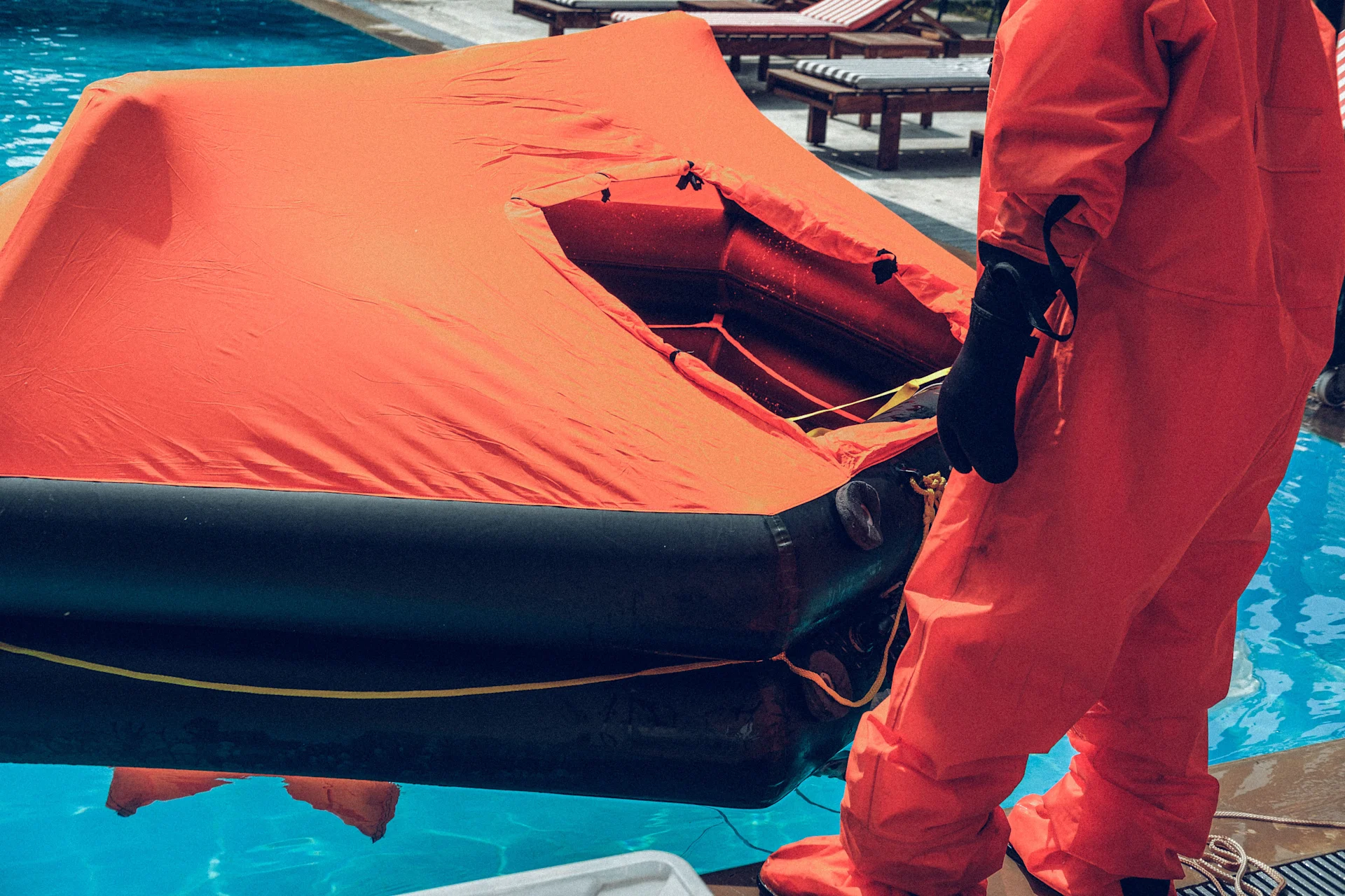 A person in a survival suit standing beside an inflated life raft during a training exercise, emphasising safety preparedness and emergency response techniques in maritime environments.