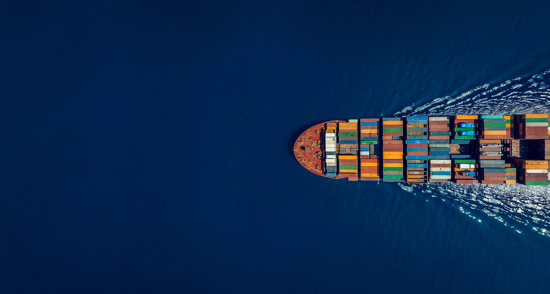 An aerial view of a container ship sailing through open waters, carrying multicoloured containers, symbolising global trade, logistics, and maritime transport efficiency.