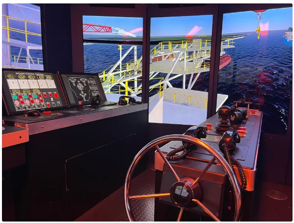 This image shows a maritime simulator setup, featuring a ship's control console with steering wheel, throttles, and control panels. Surrounding screens display a detailed offshore structure, simulating a realistic marine environment for training purposes.