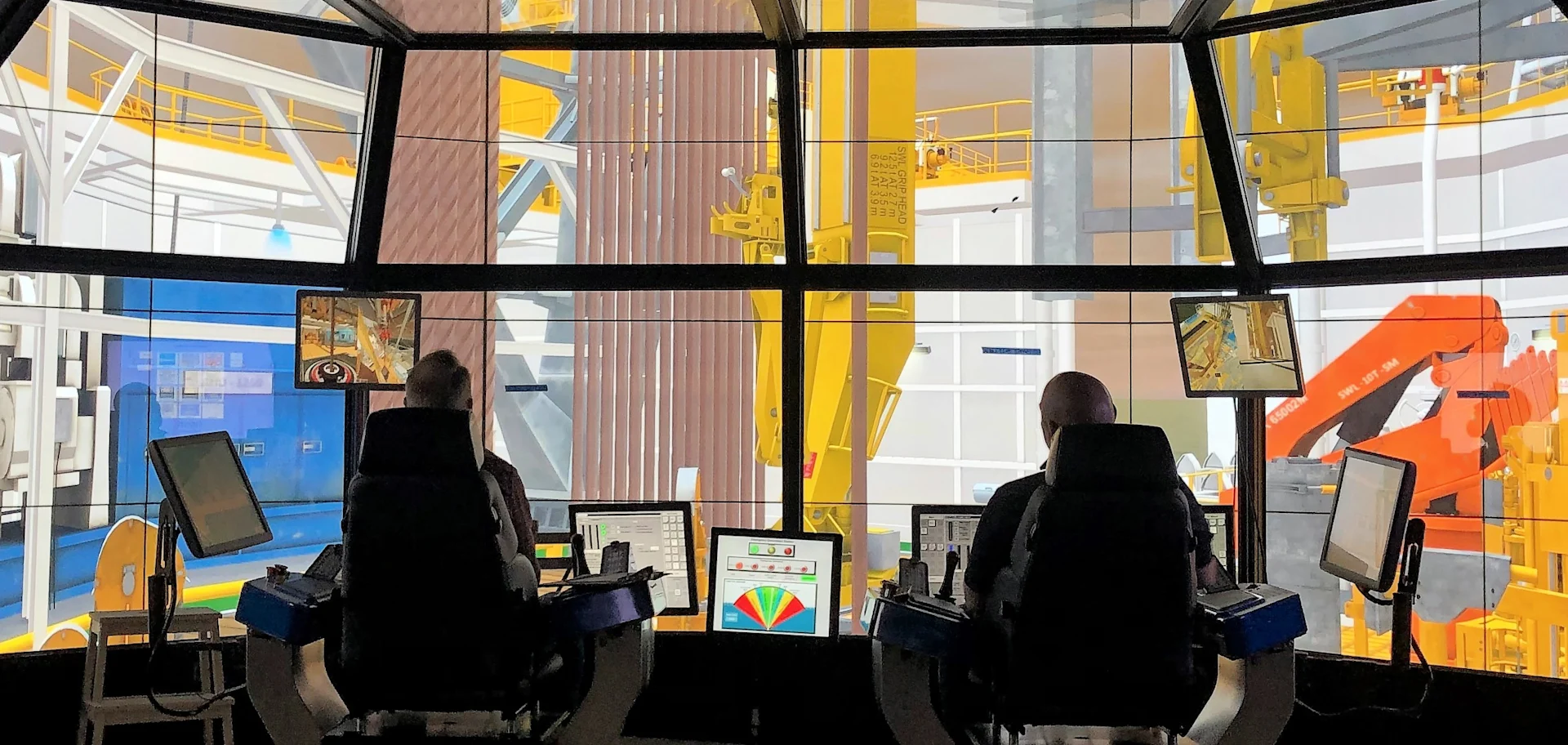 Two operators seated in a high-tech control room, managing and monitoring complex machinery, highlighting precision and control in industrial operations using advanced simulators.