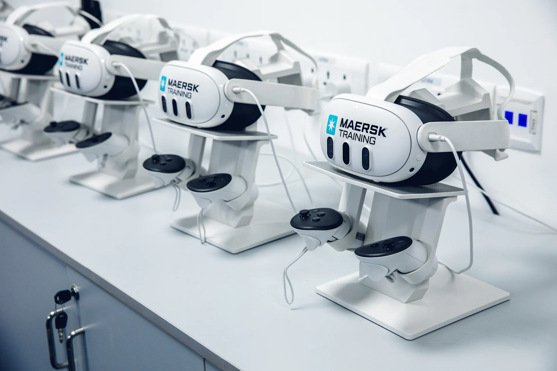 virtual reality (VR) headsets branded with "Maersk Training," neatly arranged on stands. 