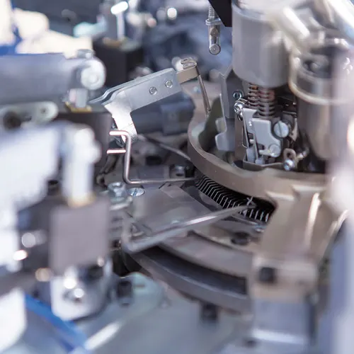 Primo piano di macchinari intricati con ingranaggi metallici, leve e molle, che mostrano un complesso sistema meccanico in tonalità argento e grigio.