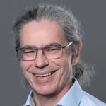 Portrait von Markus Mayer mit blauem Hemd vor Metallhintergrund