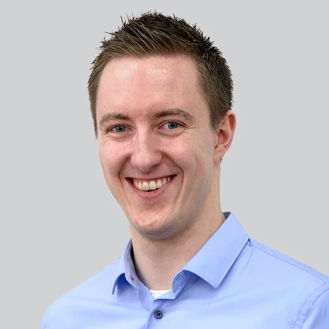 Ein junger Mann mit blauem Anzug lächelt freundlich in die Kamera.