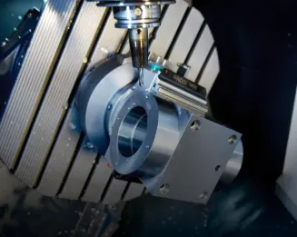 CNC-Fräsmaschine schneidet ein Metallwerkstück auf einem Lamellentisch mit Präzisionswerkzeugen und sichtbarem blauen Kühlmittel