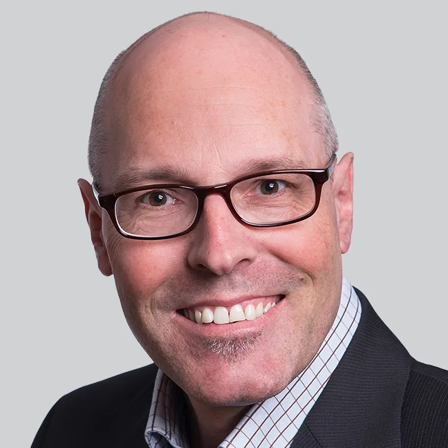 Ein Mann mit Brille und blauem Anzug lächelt freundlich in die Kamera.