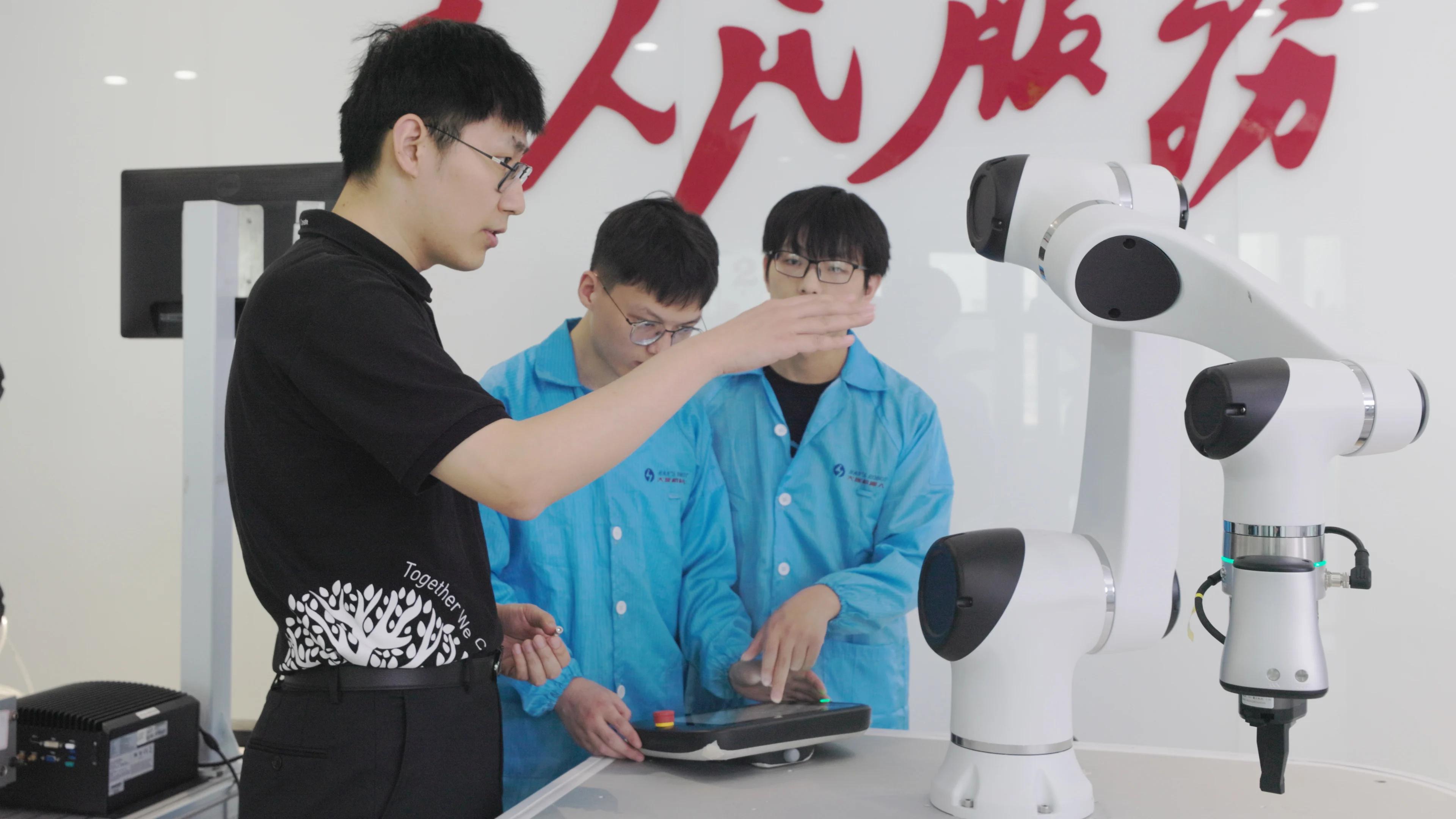 三人穿著黑色和藍色襯衫,在實驗室環境中檢查桌上的白色機械手臂。