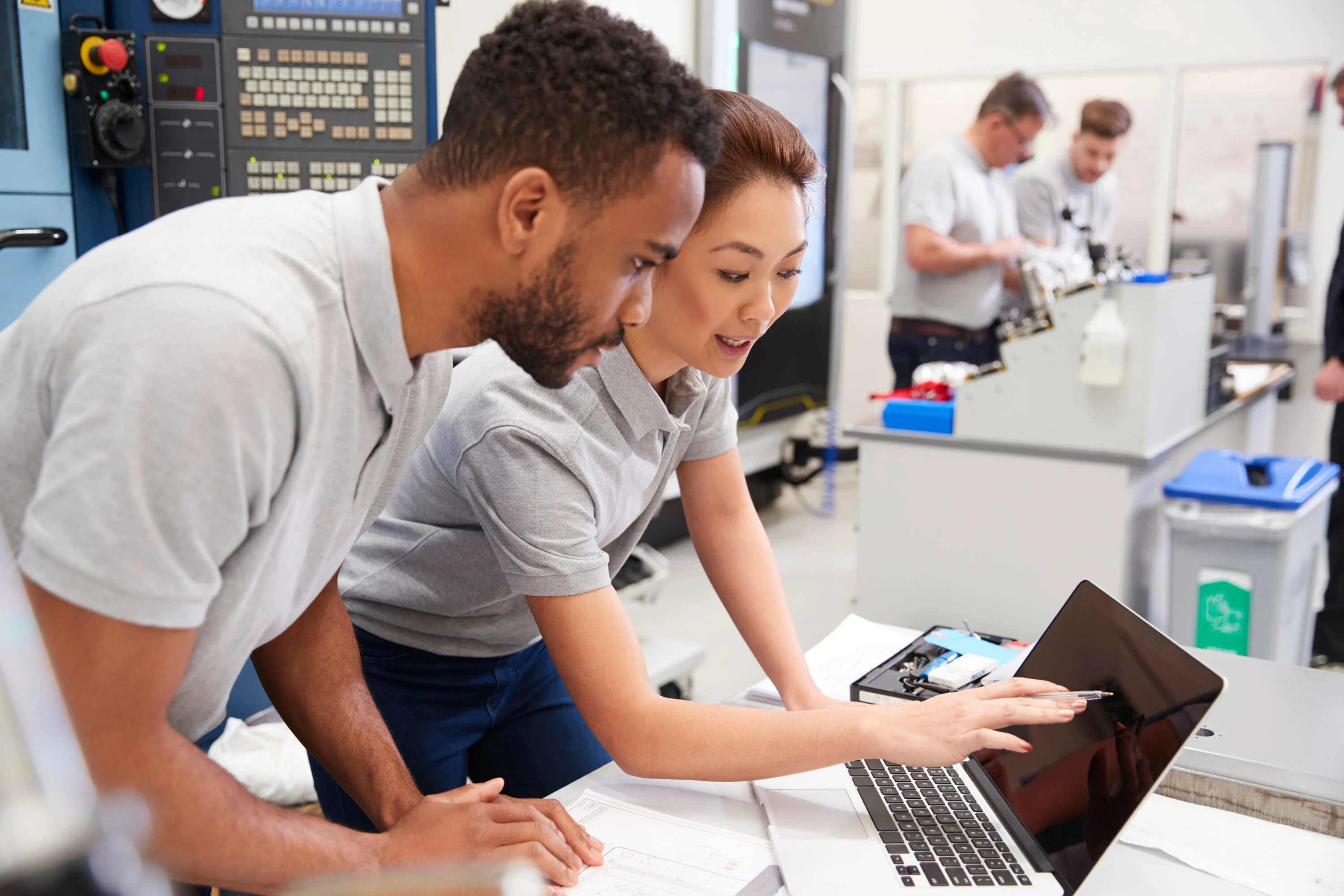 Two engineers chatting and reviewing test results together on a laptop in a technical laboratory.