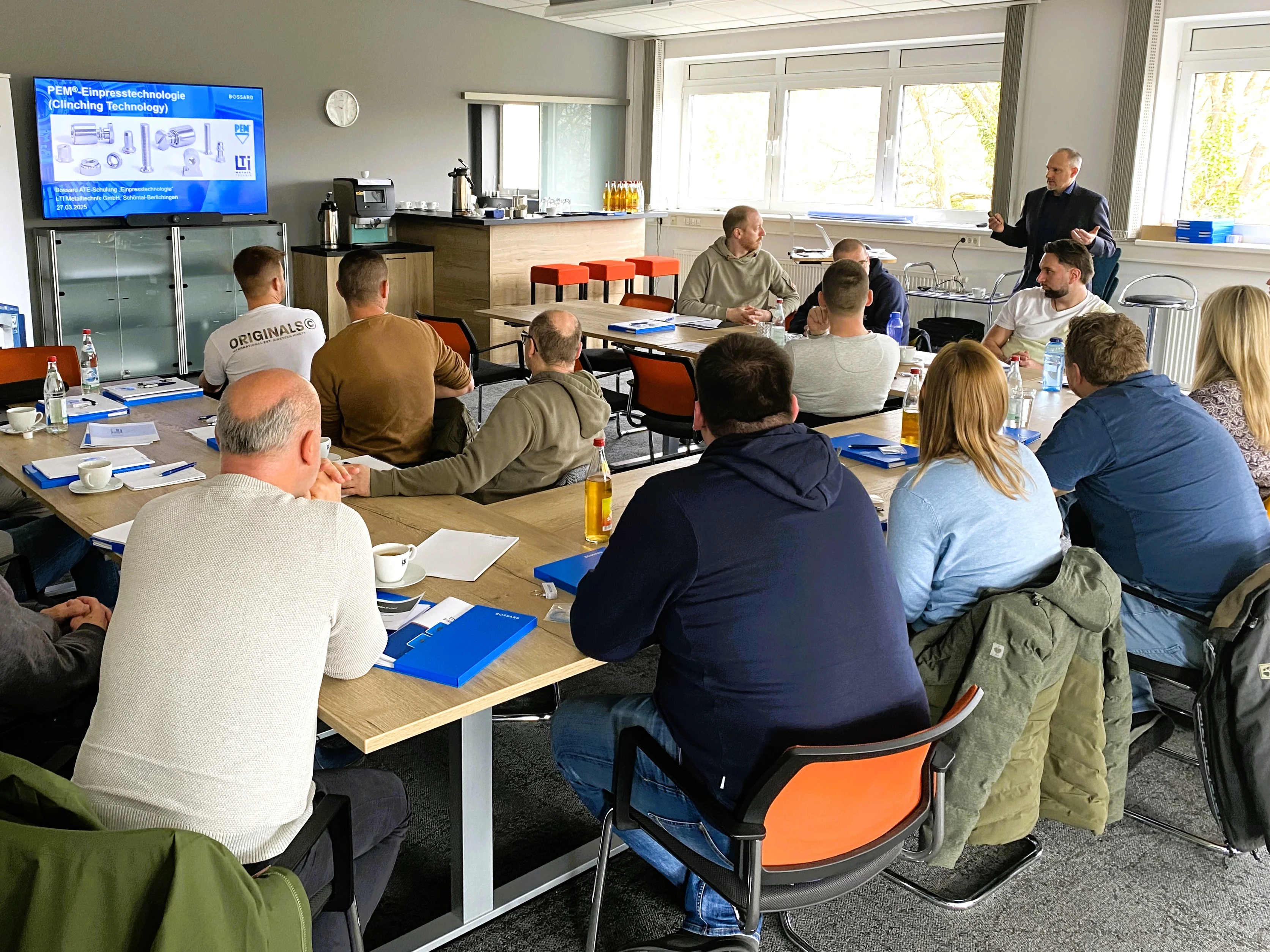 Ein Vortragsraum mit mehreren sitzenden Teilnehmern, Matthias Kreuter steht vor einer Präsentationsleinwand
