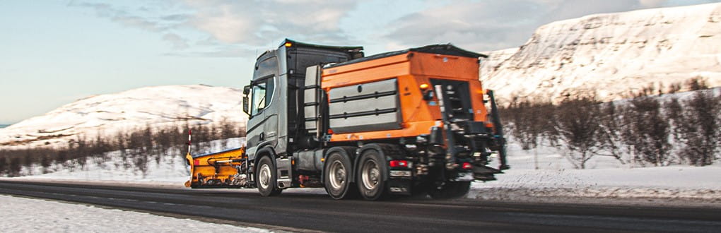 
Epoke Winterdienstgeräte sind auf der Straße neben den schneebedeckten Bergen unterwegs.