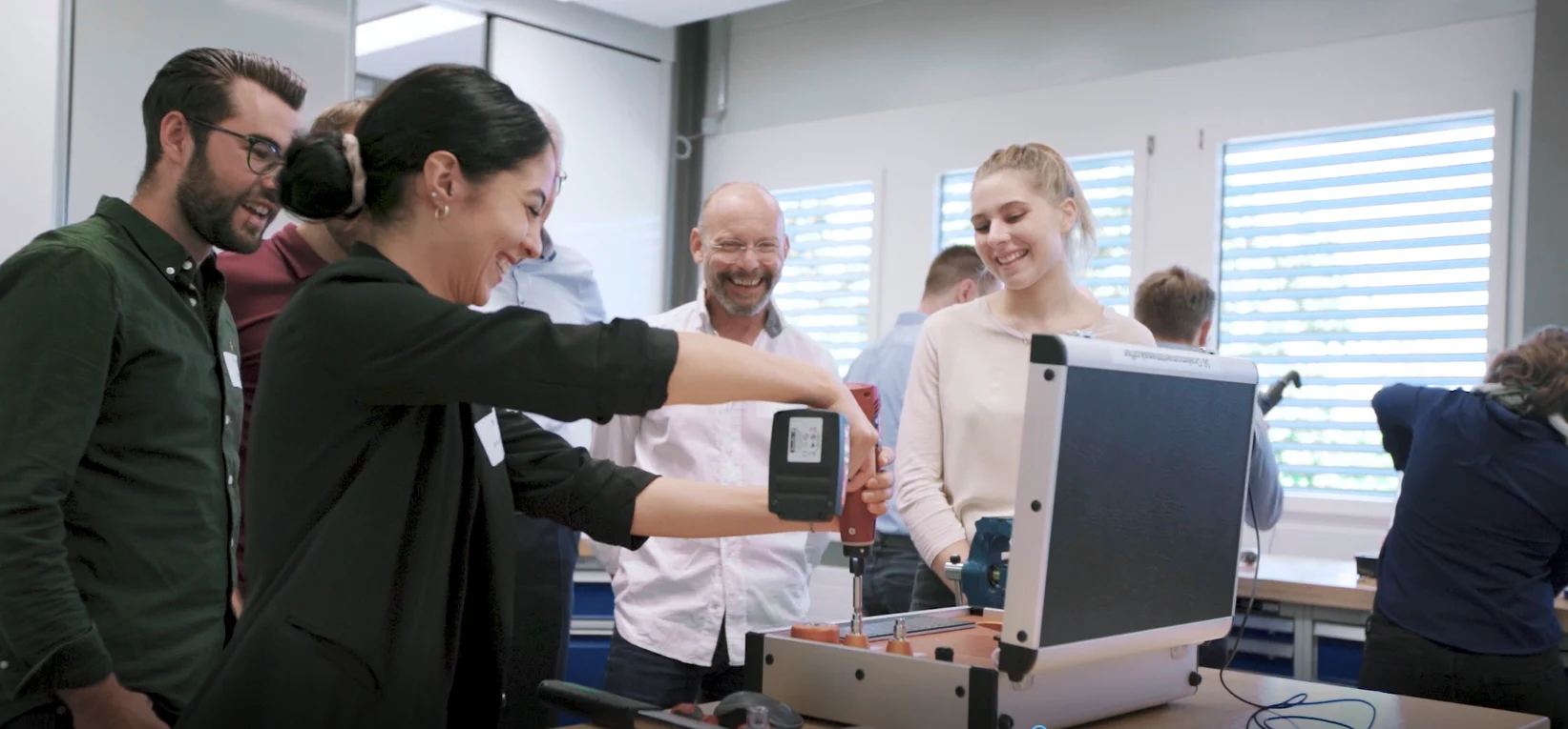 Eine Gruppe von Personen steht um eine Werkbank und benutzt Werkzeuge und einen kabellosen Schraubenzieher auf der Werkbank.