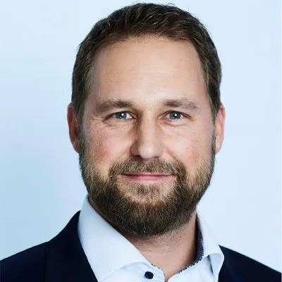 Portrait von Florian Heuter. Er trägt ein schwarzes Sakko über hellblauem Hemd.