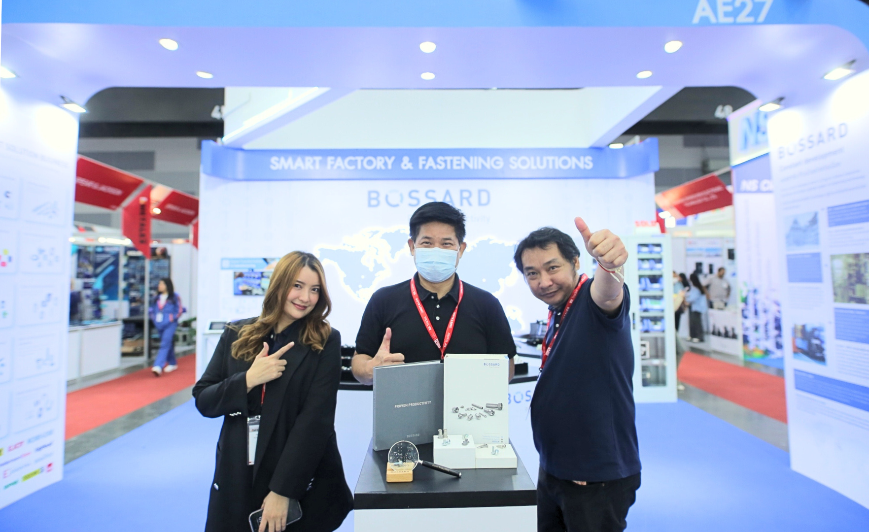 Három Bossard alkalmazott egy vásári standnál, egy "Smart Factory & Fastening Solutions" feliratú stand előtt, Bossard márkajelzéssel.