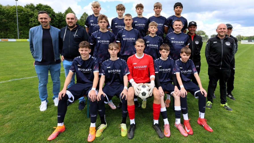 Jugendfußballmannschaft der TSG Achstetten mit Trainern in neuen dunkelblauen Bossard-Trikots auf dem Fußballplatz.
