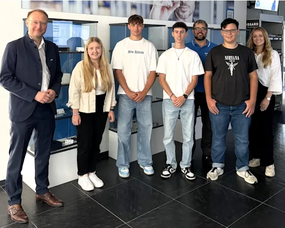 Gruppenbild von neuen Auszubildenden neben Geschäftsführer Daniel Stier, Vitrinen mit verschiedene Befestiger im Hintergrund