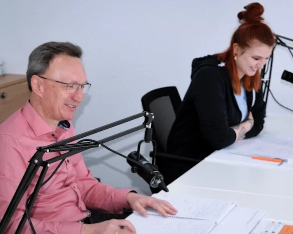 Bela Sabo and Julia Gabriel nehmen einen Podcast auf, lächeln und lesen Notizen vor Mikrofonen