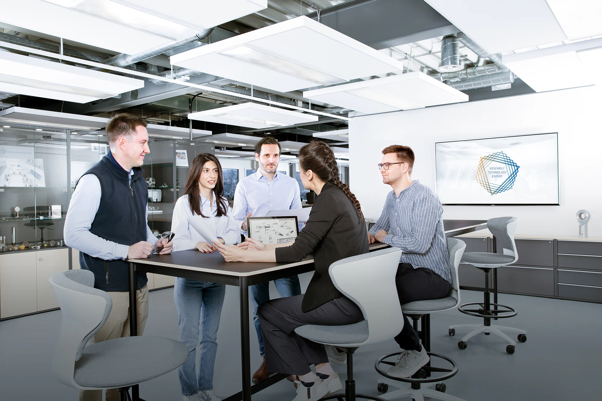 People around a table discussing a technical drawing in an industrial looking office. 