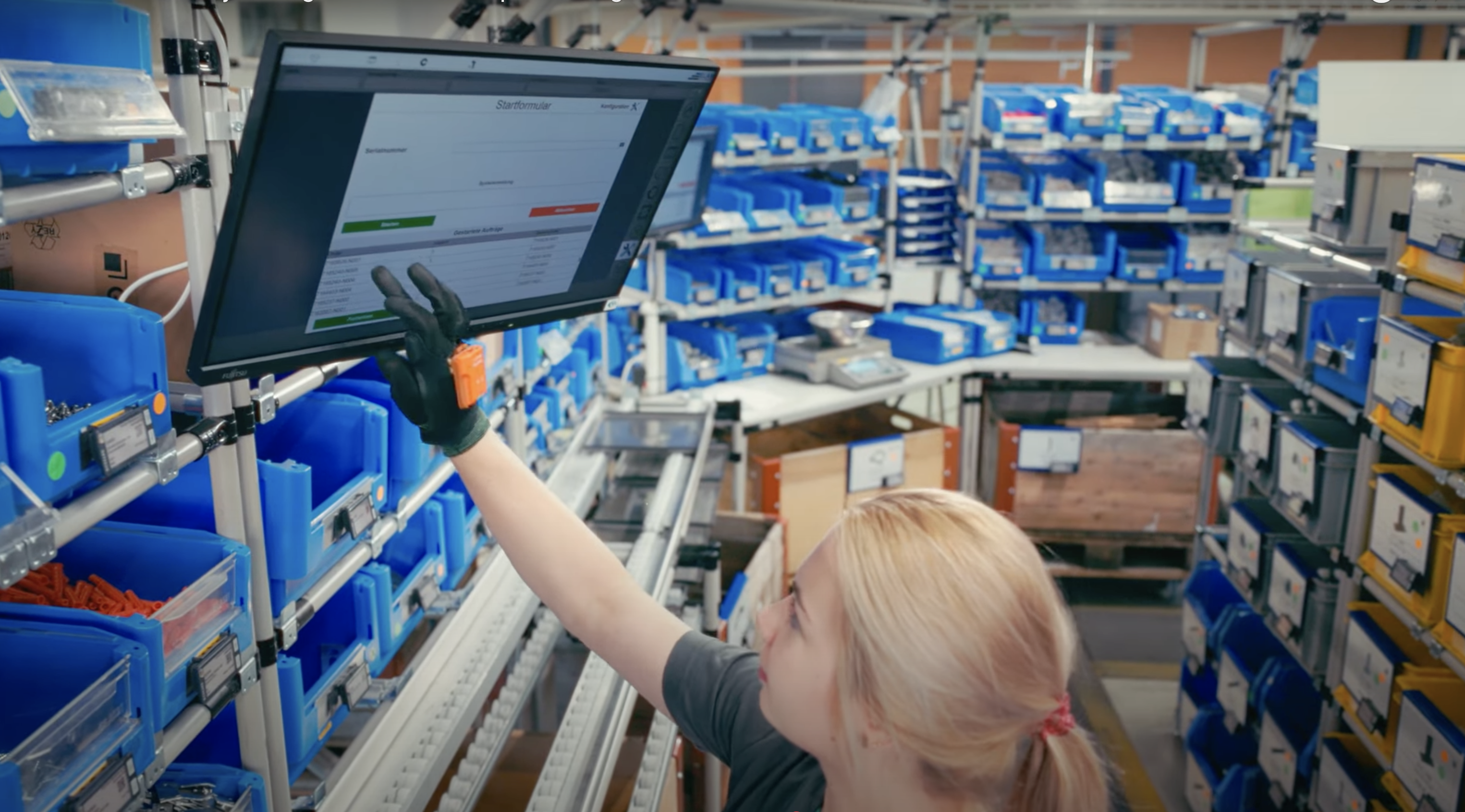 Young assembly worker checking work instructions on a computer screen with Bossard SmartBins in the background.