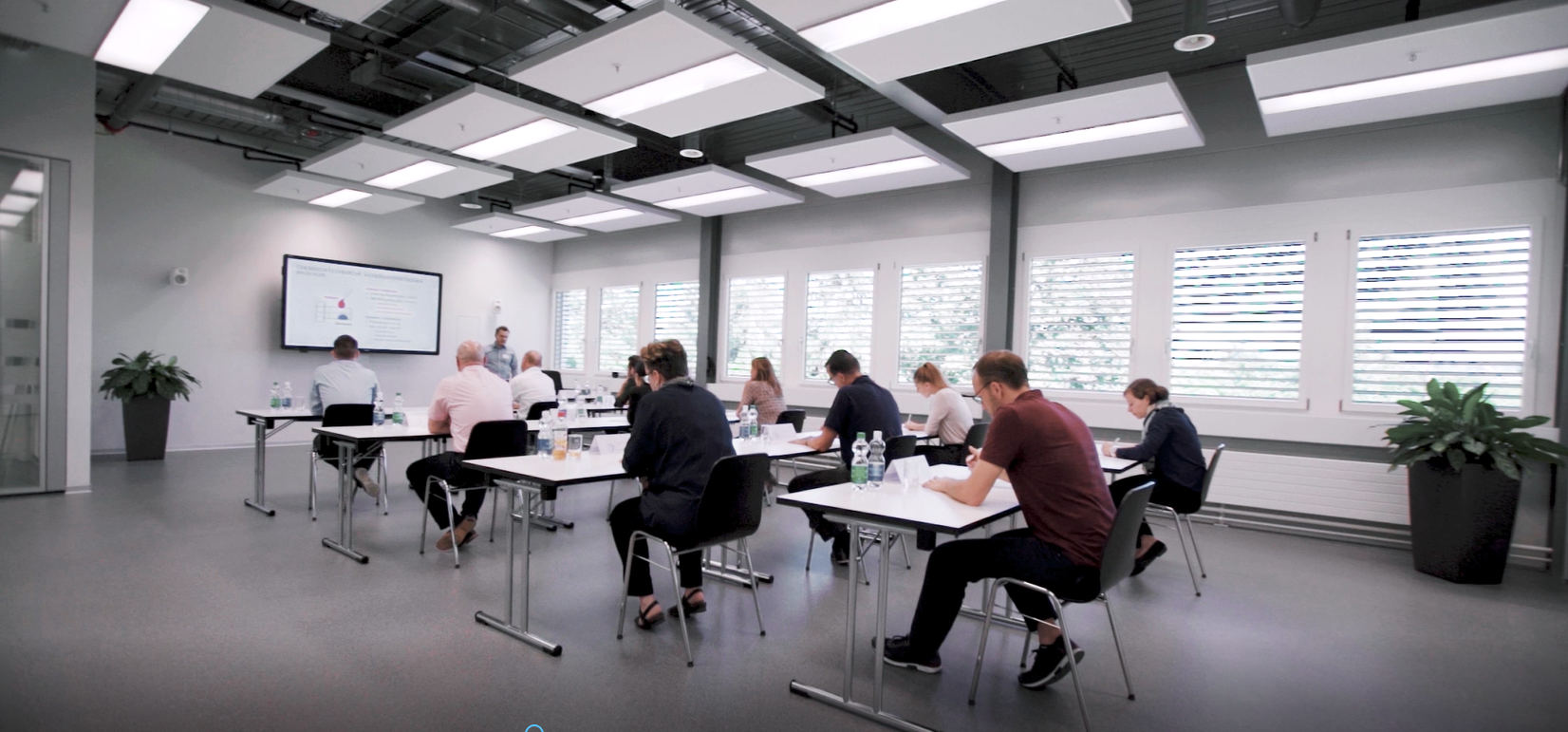  In einem Klassenzimmer sitzen Menschen an Tischen und beteiligen sich an einer gemeinsamen Diskussion.