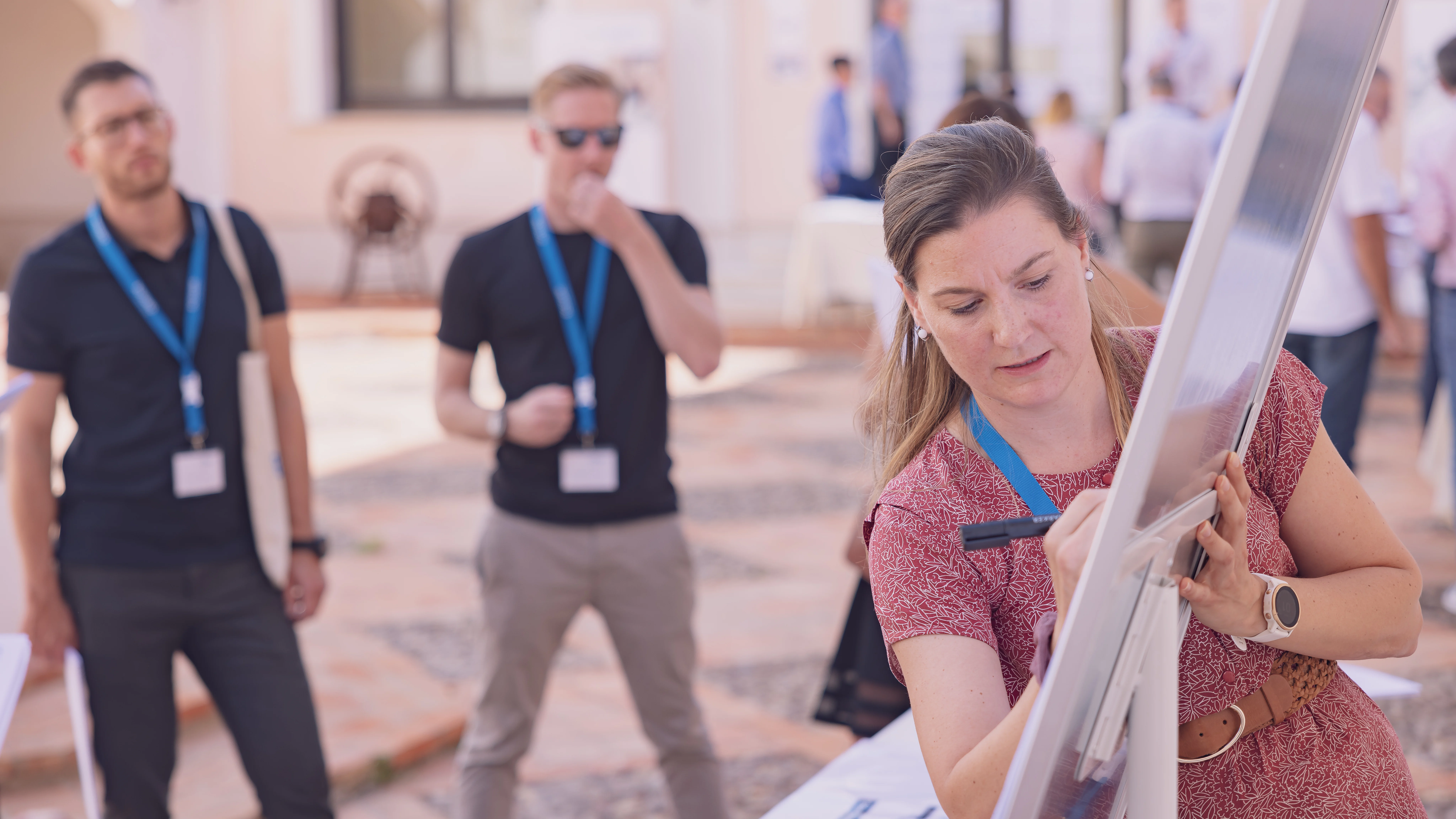 A woman is actively writing on a whiteboard, demonstrating engagement in a learning or brainstorming session.