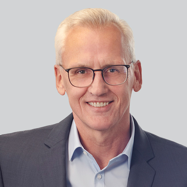 Ein Mann mit blauem Anzug lächelt freundlich in die Kamera.