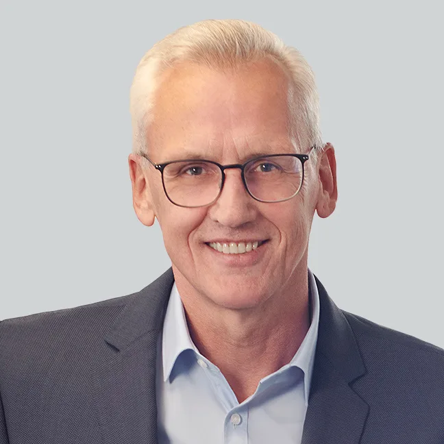 Ein Mann mit blauem Anzug lächelt freundlich in die Kamera.