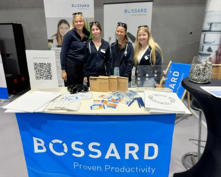 Vier junge Auszubildende am Bossard-Messestand mit Produktmustern, Giveaways und gebrandetem Hintergrund.
