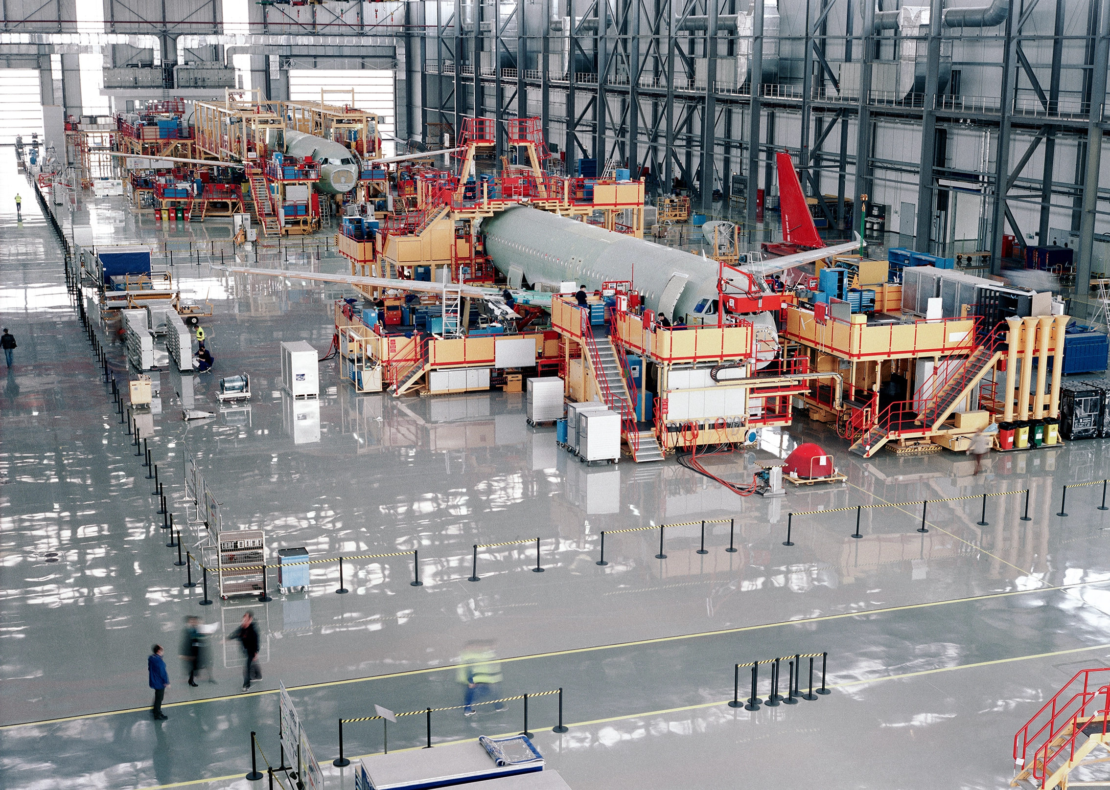 Et stort fly bliver samlet inde i en rummelig fabrik, hvor industrielt maskineri og arbejdere ses i baggrunden.