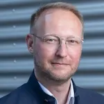 Portrait von Daniel Stier mit Bart, kurzes Haar, freundliches Lächeln.