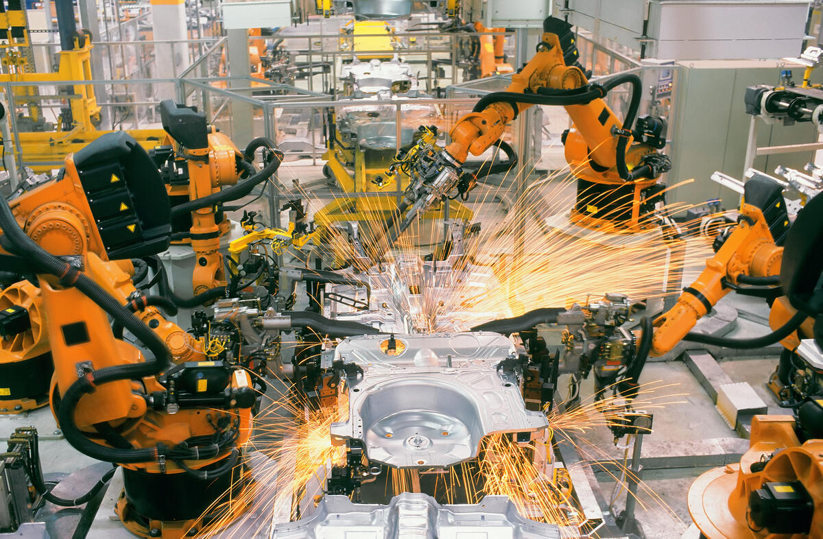 Orange industrial robots welding metal car parts in a factory, creating bright sparks on an automated assembly line.
