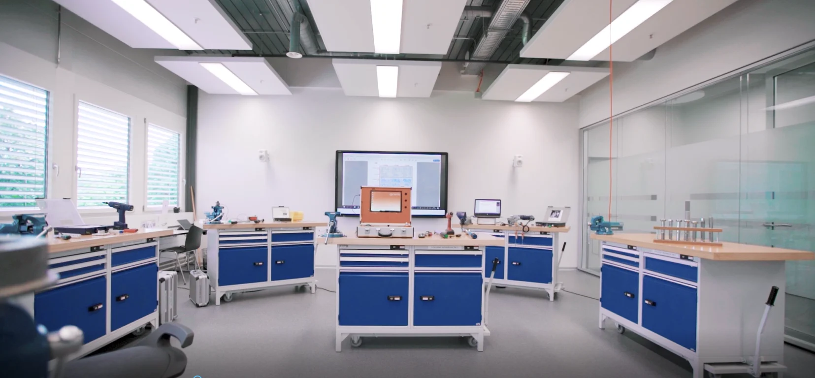 Ein Klassenzimmer mit blauen Werkbänken und weissen Wänden, das eine helle und einladende Lernumgebung schafft.