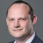 Portrait von Daniel Schäfer mit Glatze, freundliches Lächeln, dunkler Hintergrund.