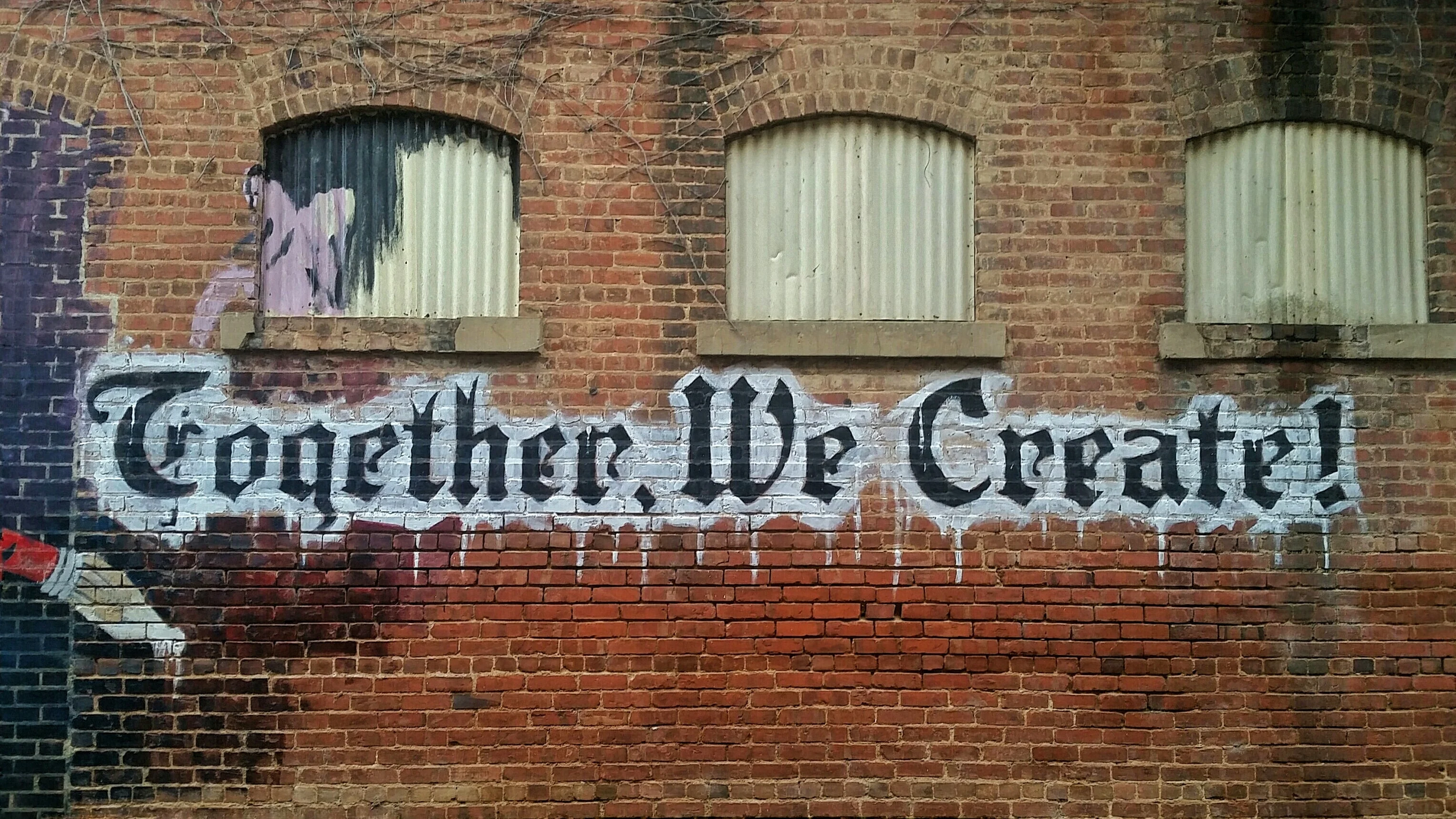 A textured brick wall featuring black and white graffiti that reads "together we create!" in an artistic style.