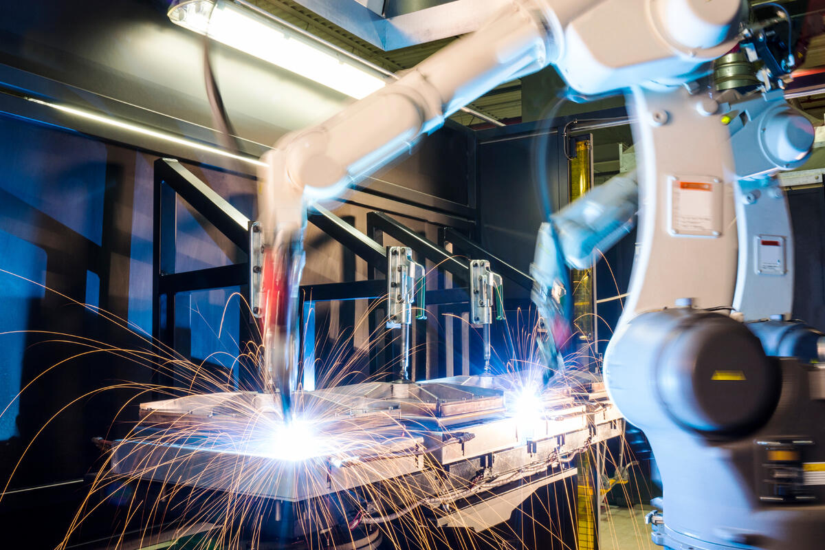 Industrial robotic arms welding metal with bright orange sparks flying in a modern automated manufacturing facility.