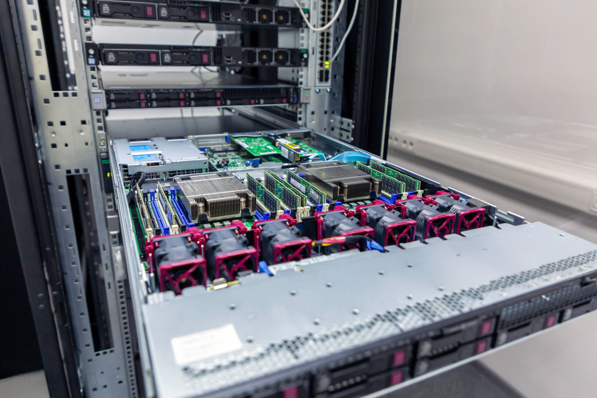 Rack de servidor interior mostrando placa base con ranuras RAM, disipadores de calor y ventiladores de refrigeración rojos montados en un chasis de centro de datos