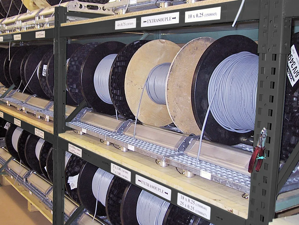 Industrial shelving unit storing large cable reels with white and black wire spools organized on metal racks with labeled sections.