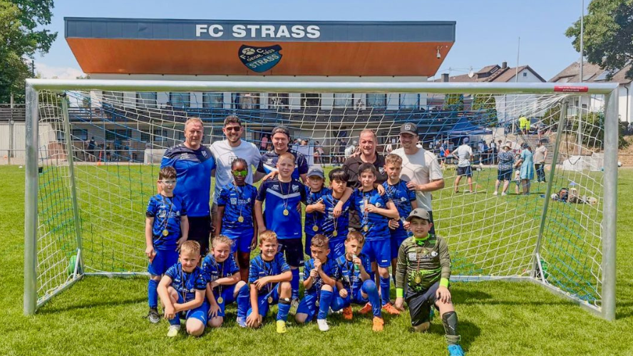 Jugendmannschaft des FC Strass mit Trainern vor einem Fußballtor nach einem Turnier, mehrere Spieler tragen Medaillen.