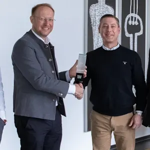 Zwei Männer schütteln sich die Hände und halten eine Auszeichnung