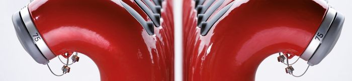Zwei Reihen roter Hydranten mit silbernen Kappen und Nummern, seitlich betrachtet, die ein symmetrisches Muster bilden.