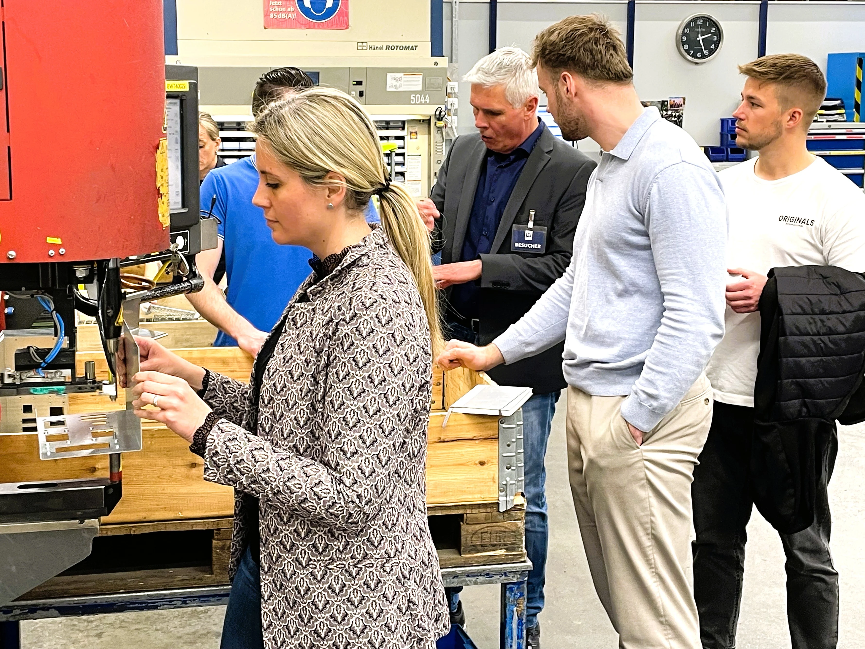 Montagehalle mit mehreren Workshopteilnehmern, blonde Frau bedient eine Haeger Einpressmaschine mit Musterteilen